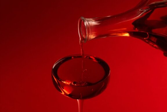 Red cocktail being poured from red bottle into red glass.