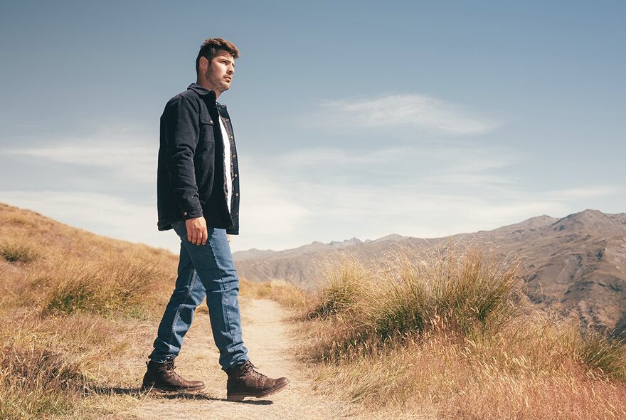 A man walking across a track in a dry, desolate area. 