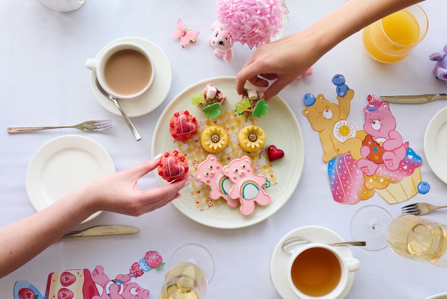 Care Bears themed high tea treats, including bear-shaped cookies with pink icing alongside cups of tea and juice.