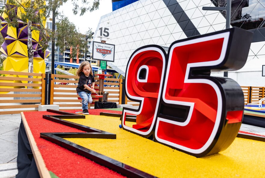 Child playing a minigolf game featuring the name 95 and red and yellow colours.