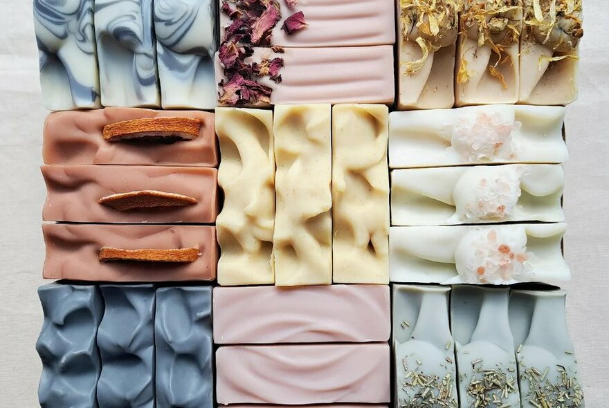 Hand-made bars of soaps placed together in blocks of three creating a grid pattern of varying colours.