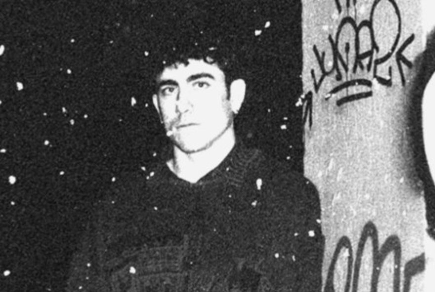Hazy black and white photo of musician Louis Smith standing next to a wall with some graffiti.