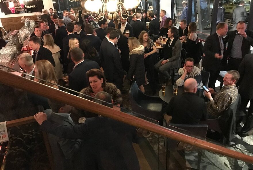 Crowded restaurant with people in suits seated at tables.