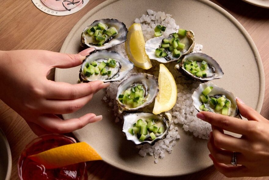 Looking down on a plate of seven oysters with a green dressing and lemon wedges.