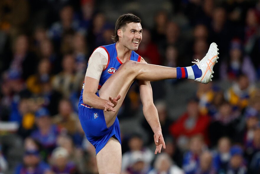 A Western Bulldogs AFL football player with his leg in mid-air having just kicked an out of sight football, during a match.