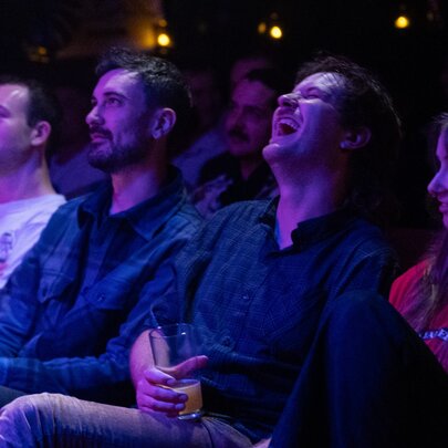 Four people seated in a row under dark purple lights, one person laughing.