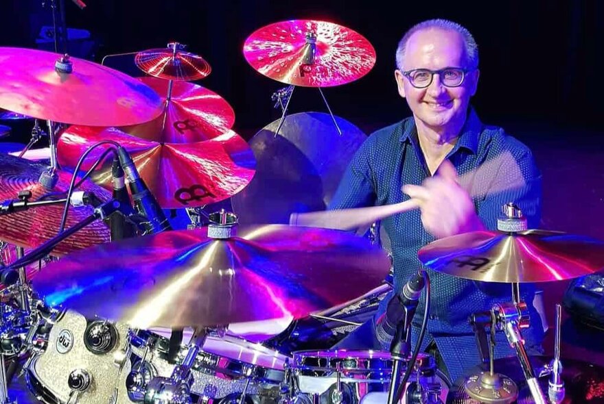 A smiling man playing a very large drum kit. 