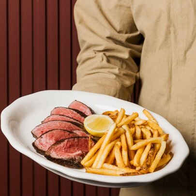 A waiter holding a white plate of steak frites, a classic French meal consisting of beefsteak paired with french fries.