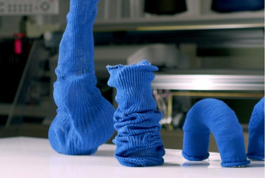 Blue 3D tubular knitting samples on a white bench in an industrial space.