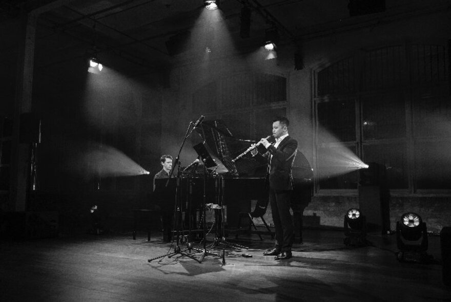 Pianist and oboe player performing under angled lighting in a dark space.