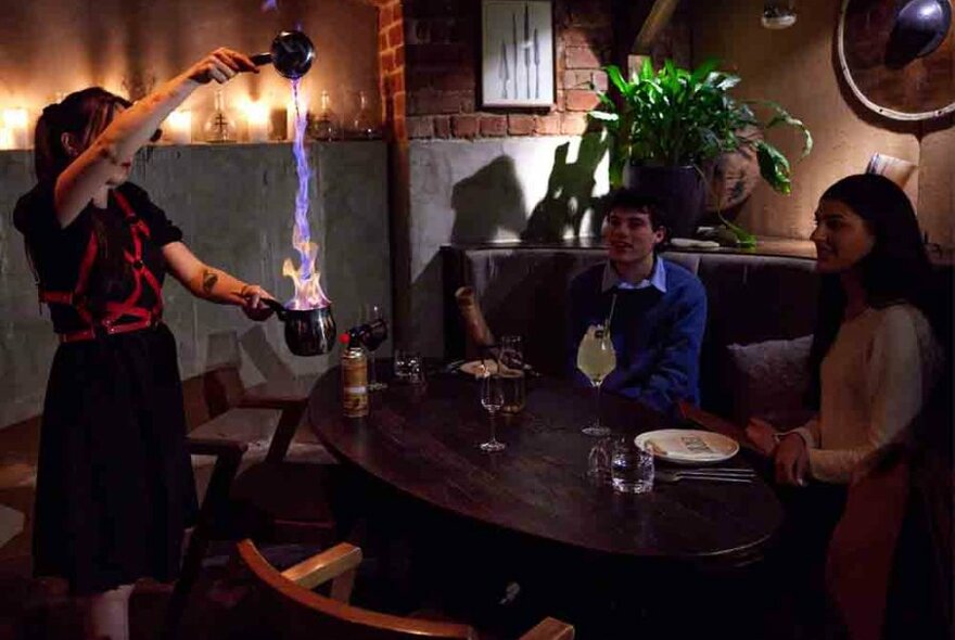 A bartender making a cocktail by pouring a stream of fire into a goblet.