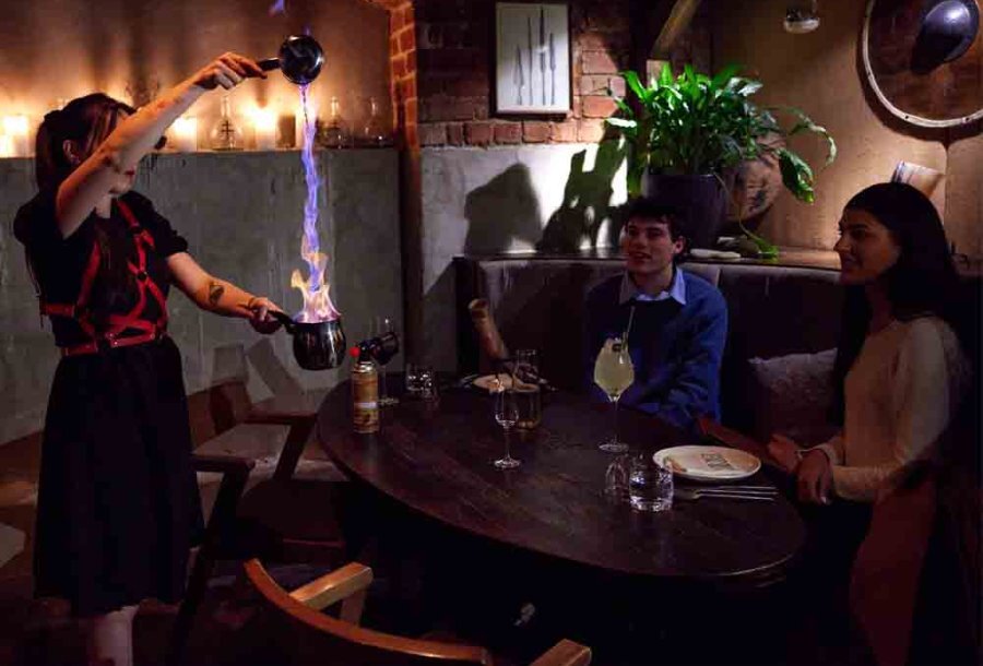 A bartender making a cocktail by pouring a stream of fire into a goblet.