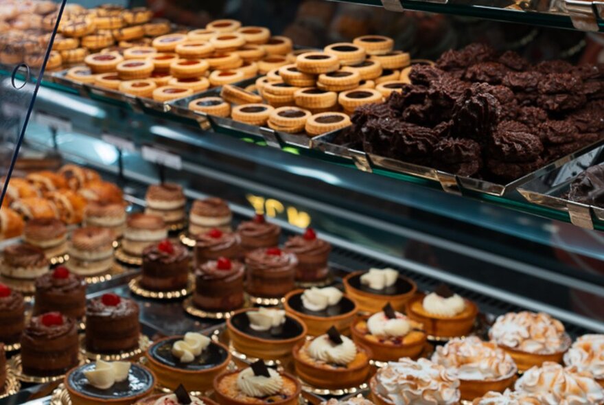 Trays of sweet biscuits and mini desserts in a food display cabinet.