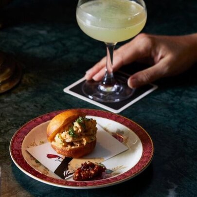 A cocktail on a marble topped table, with a small plate of food next to it.