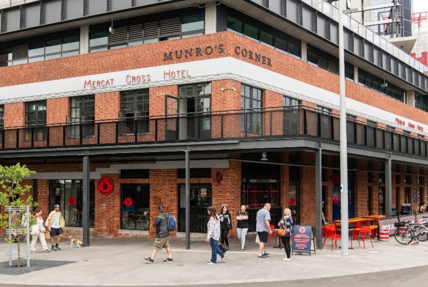 Exterior of Brick Lane Market showing a corner site of a red brick building, passersby on street level, and an outdoor balcony.