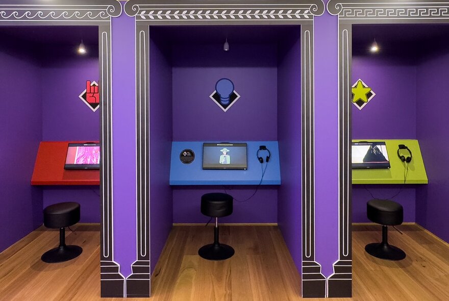 Three purple gaming booths with different coloured monitors and headsets. 