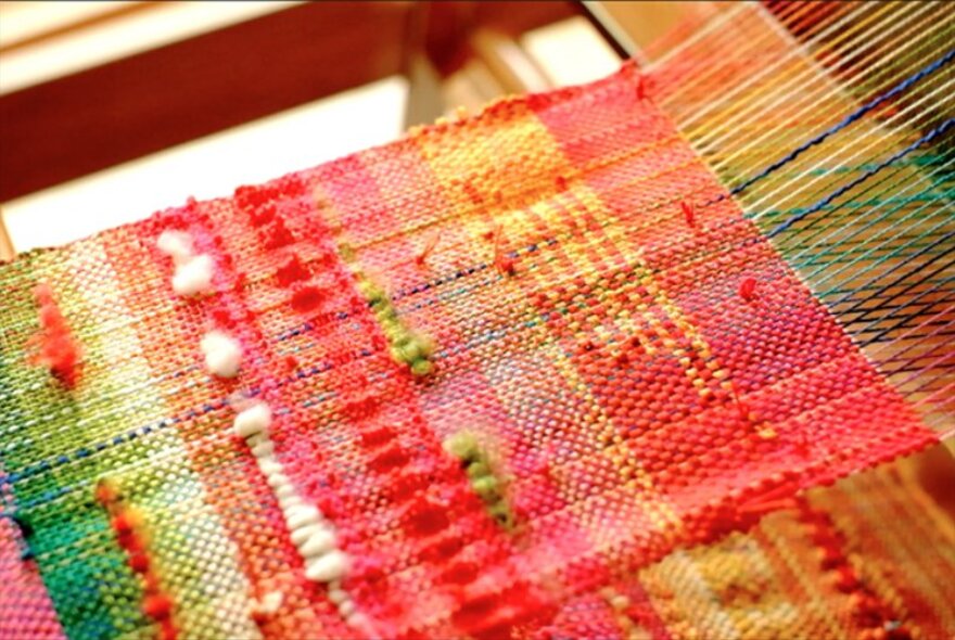 A piece of woven fabric with reds and greens, still on the loom.