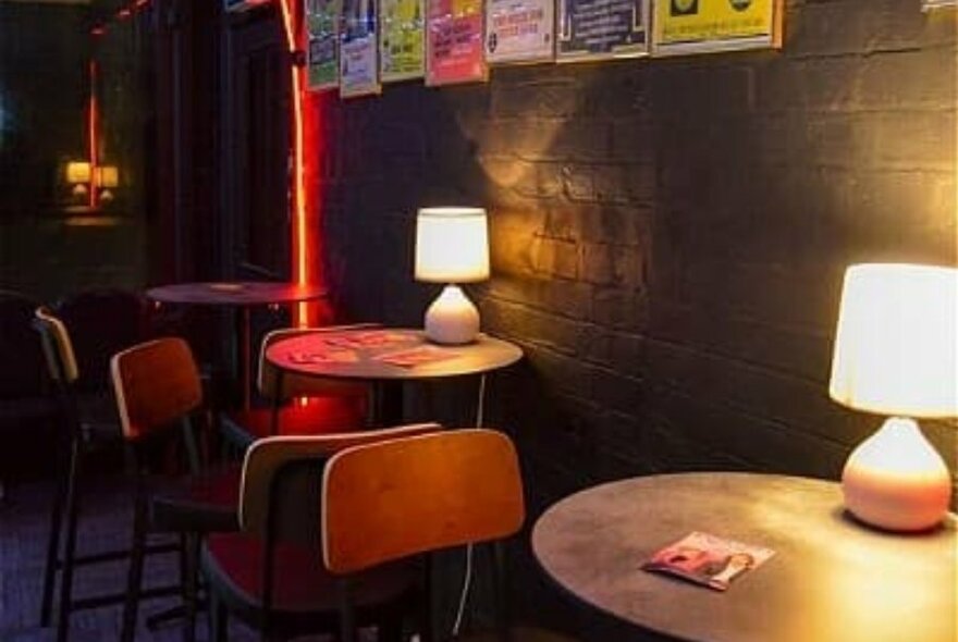 Small tables and chairs with lamps in a row against a wall.