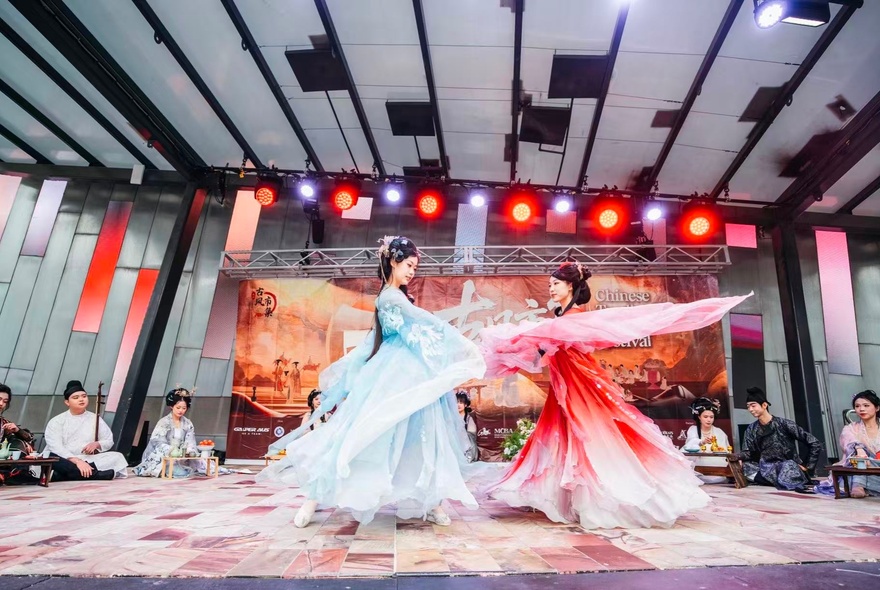 Female performers in Chinese flowing costumes on stage at a cultural festival.