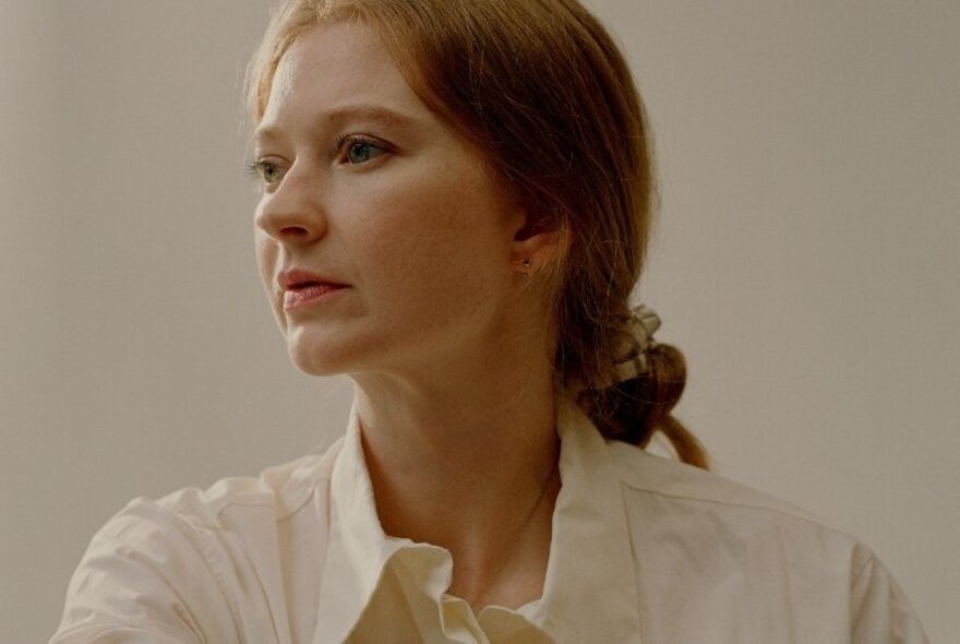 Author Bri Lee, a woman wearing a white shirt, her brown hair pulled back into a loose bunch behind her head.  