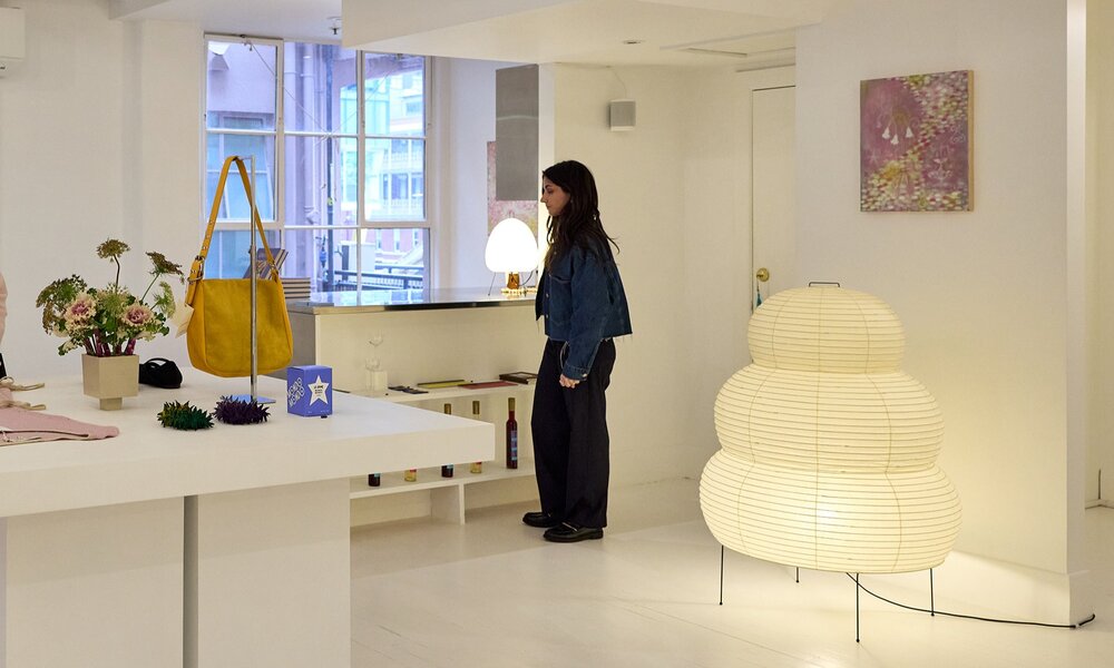 A woman browsing in a boutique with accessories and a large Akari lamp.