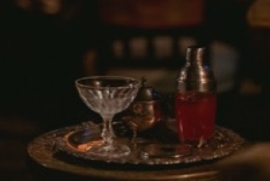 A glass and a cocktail shaker on a silver tray.