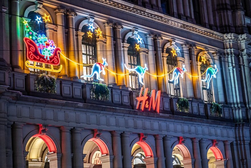 A Christmas sleigh pulled by kangaroos in neon lights on a building facade