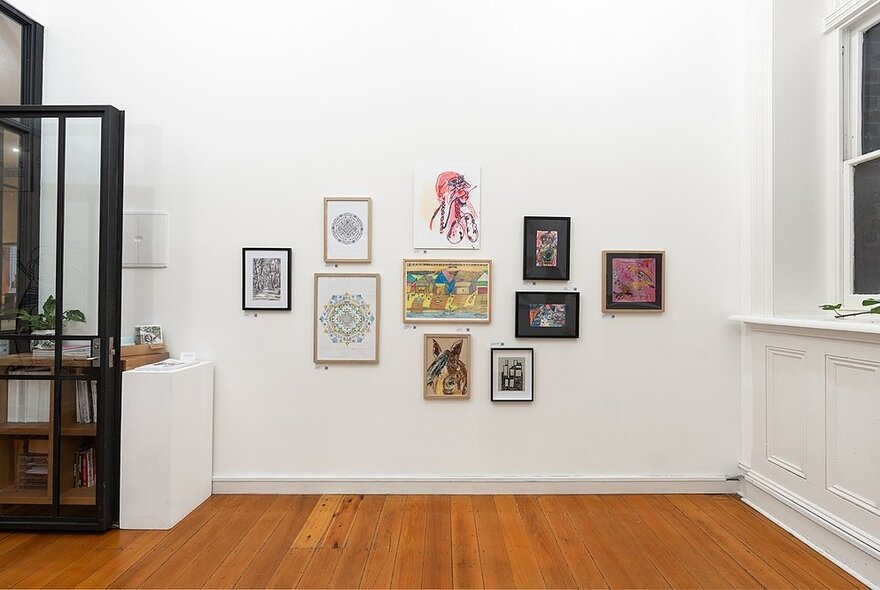 An art gallery space with small framed pictures on the wall arranged randomly. 