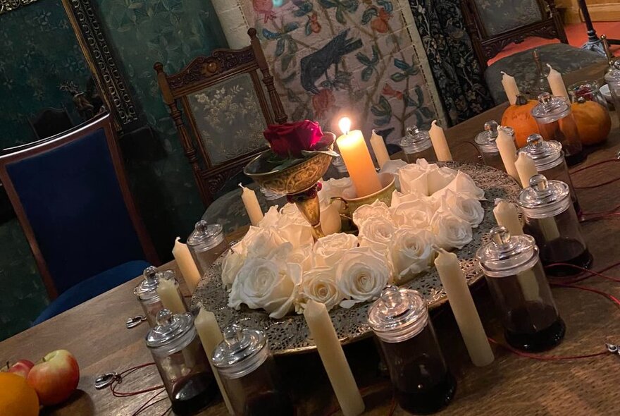 White lit candles arranged around a table centrepiece of white roses in a low bowl.