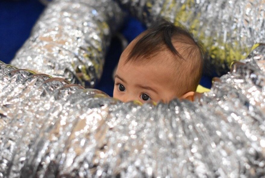 A baby peeping out of some silver industrial tubing.
