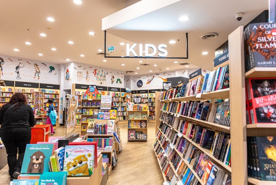 Inside Dymocks Melbourne with shelves full of books and a large sign hanging from the ceiling saying KIDS.