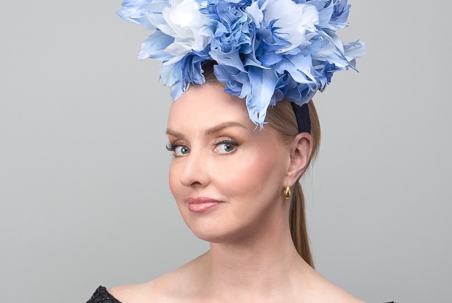 Headshot of a woman modelling a blue and white floral fascinator. 