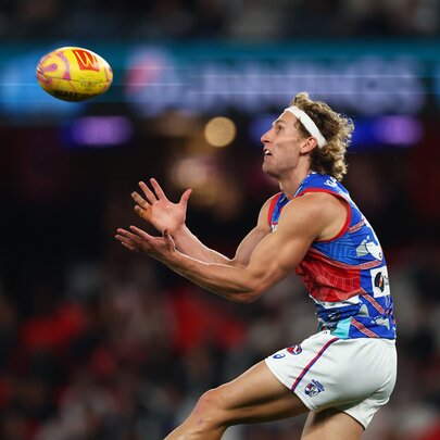 A Western Bulldogs AFL player jumping up to mark a football that is in mid-air heading towards him.