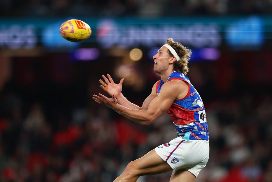 A Western Bulldogs AFL player jumping up to mark a football that is in mid-air heading towards him.