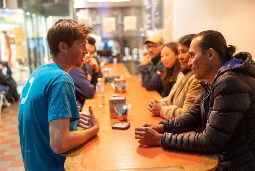 A group of people seated at a long table in a casual restaurant, waiting for food.