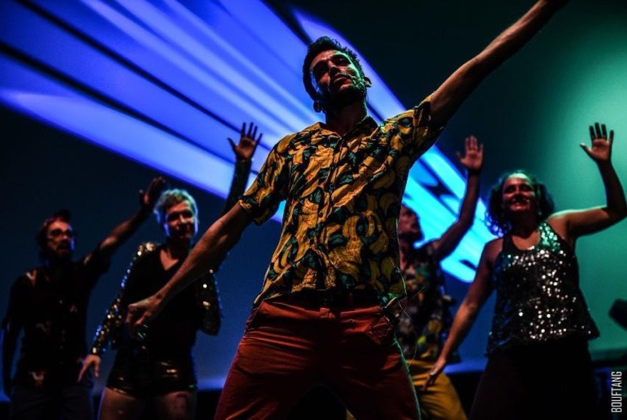 Performers on a stage dancing, with a blue spotlight in the background.