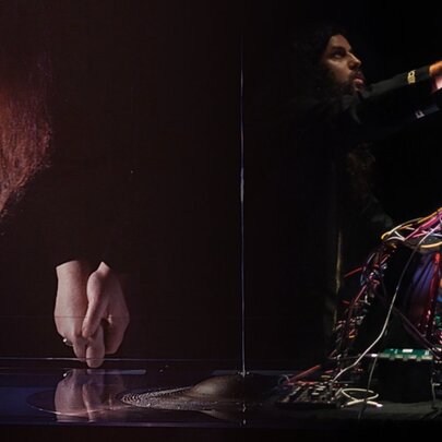 Sound artists Ros Bandt and Vijay Thillaimuthu performing live with electronic equipment in a dark venue.