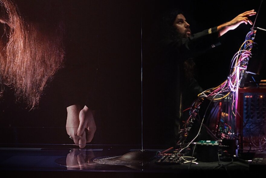 Sound artists Ros Bandt and Vijay Thillaimuthu performing live with electronic equipment in a dark venue.