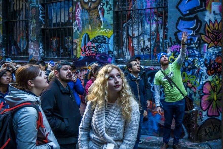 Tour guide talking to a group of people and pointing to street art in a Melbourne laneway.