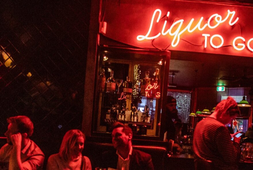 The darkened interior of a bar, lit up only by a red neon sign.