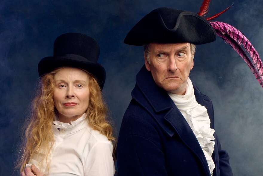 Two actors in period dress wearing hats and frilled shirts.