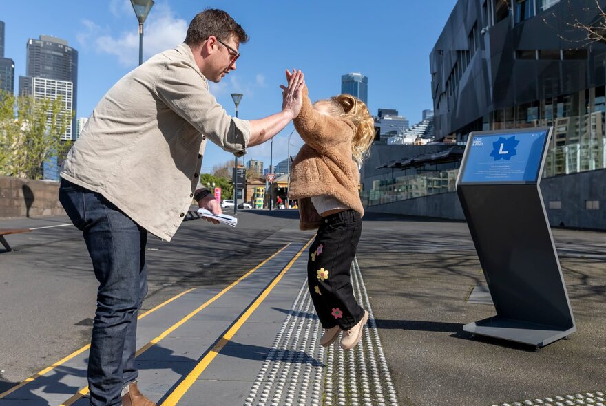 Adult and child high-fiving while standing on steps at Fed Square.
