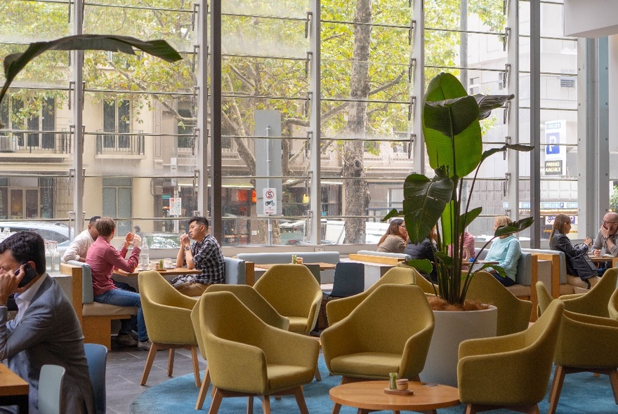 Interior of Axil Coffee Lonsdale St, with people seated in club chairs next to large windows, enjoying coffee.