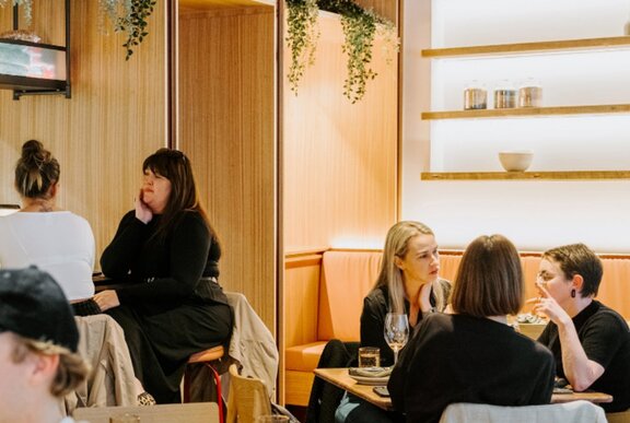 People seated at tables in a lightly lit restaurant with wood details.