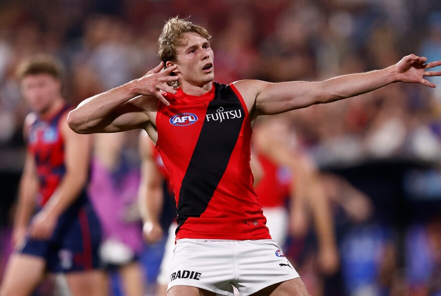 Essendon AFL player with arms oustretched during a game.