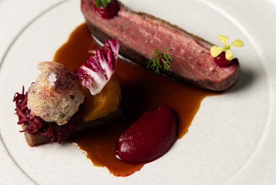 A large white plate with a fillet of medium rare beef resting on a dark sauce with a vegetable side.