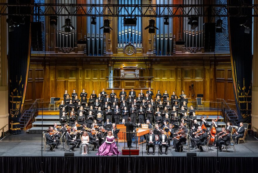 A full orchestra organised on stage with a grand organ behind them. 