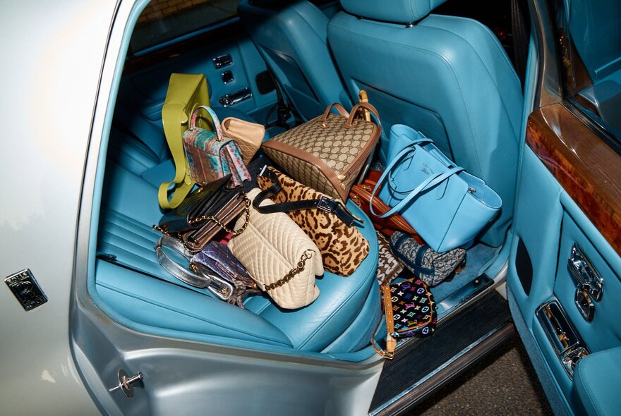 An open car door showing aqua coloured leather upholstery and lots of designer bags. 