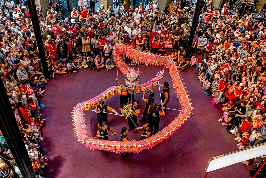 Looking down on a lion dance, showing performers operating the puppet and people crowded around in a circle. 