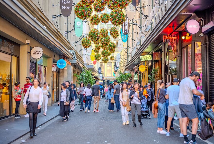 People walking through a laneway with festive floral decorations overhead.